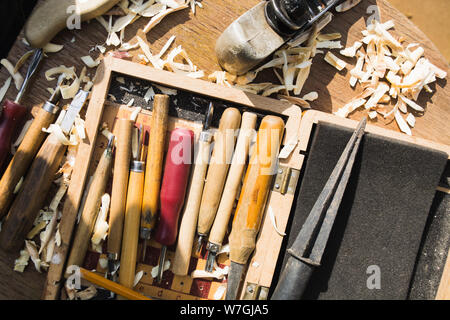 Numerosos cortadores y herramientas para la talla en madera en caja de madera con virutas de madera. Sentar planas. Vista superior