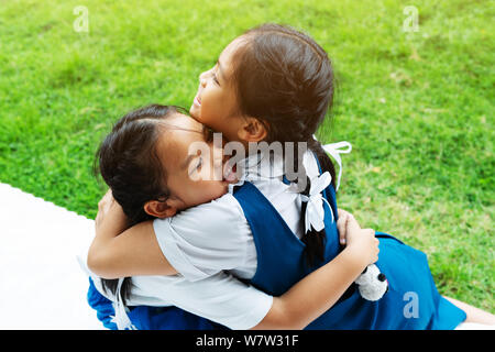 Dos pequeños asian girls hermanas abrazos feliz post en uniforme escolar, concepto de vuelta a la escuela Foto de stock