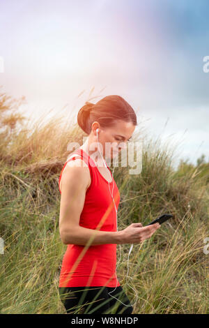 Mujer con auriculares, auriculares, controlar su teléfono móvil después de hacer ejercicio en el exterior Foto de stock