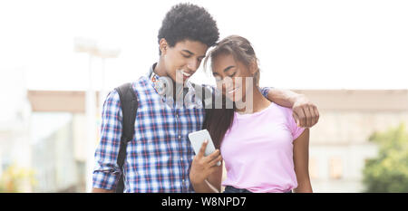 Los adolescentes sonriente mirando a la pantalla del smartphone mientras camina al aire libre
