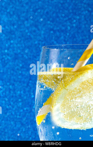 Soda fresca con burbujas un cubito de hielo, una rodaja de limón y una pajita en un fondo azul brillante