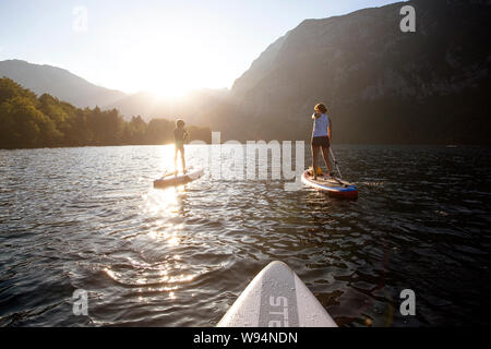 Madre e hijo remando en sup en el manantial de aguas color esmeralda del lago alpino de Bohinj, Eslovenia al atardecer