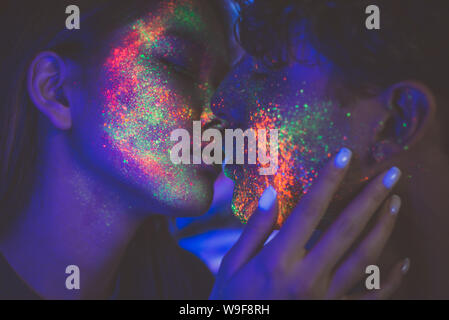 Pareja besándose en la discoteca con pintura fluorescente en la cara Foto de stock