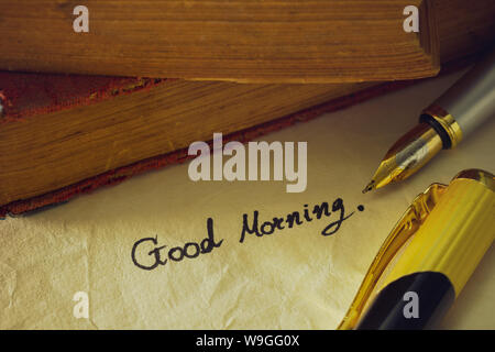 Bolígrafo de latón Vintage escrito ' Good morning ' sobre papel antiguo y viejo libro apiladas sobre la mesa de madera.