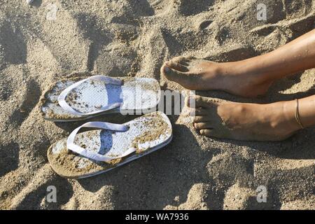 Tiro de pies femeninos cerca de chanclas en la arena