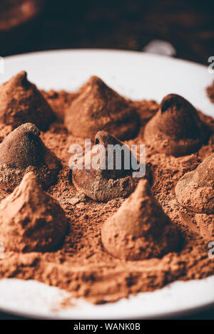 Trufas de chocolate caseras recubiertos de cacao en polvo sobre la placa blanca.
