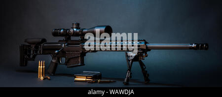 Moderno potente rifle de francotirador con una mirilla telescópica montada sobre un bipod. Munición y un almacén adicional junto al rifle. Foto de stock