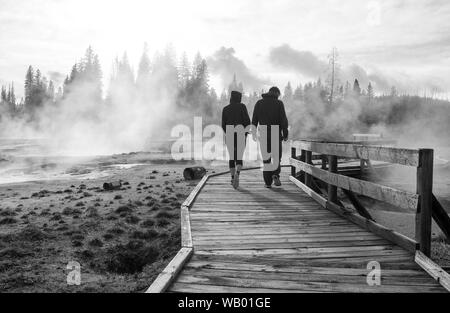 Blanco y negro paisaje abstracto con gente de pie cruzando el puente de madera en el lago del amanecer con niebla y termas en el Yellowstone National par Foto de stock
