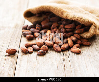 Habas de cacao crudo en arpillera bolsa sobre una mesa de madera Foto de stock