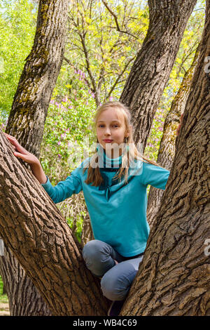 Adolescente sonriente chica rubia se subió a un árbol umbroso en el parque Foto de stock