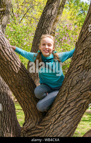 Adolescentes riéndose chica rubia se subió a un árbol umbroso en el parque Foto de stock
