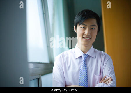 Retrato de un joven empresario de pie junto a una ventana de una oficina. Foto de stock