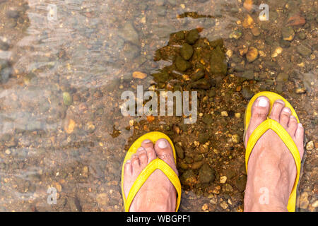 Hombre que llevaba zapatillas baño de pies en la cascada. Pies caminando en río. Los hombres vestían sandalias color amarillo Fotografía de stock - Alamy