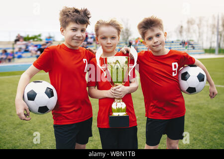Tres niños alegres feliz de deportes equipo de fútbol. Los niños Futbolistas sosteniendo el trofeo en el estadio. Los jóvenes ganadores del torneo de fútbol juvenil