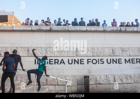 LYON, FRANCIA - Julio 14, 2019: el joven negro francés hombre sentado en las escaleras tomando un selfie con su smartphone frente a una multitud en la orilla del Foto de stock