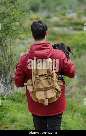 Joven con mochila lleva su perro en sus brazos Foto de stock