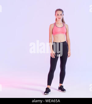 Hermosa mujer joven en pleno crecimiento en ropa de gimnasia de pie sobre un fondo de color rosa púrpura. Foto de stock