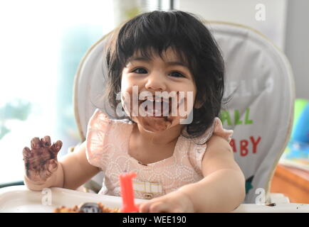 Lindo bebé niña feliz desordenado comer tarta de chocolate de cumpleaños Foto de stock