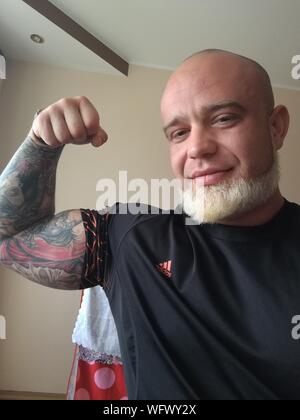 Retrato del hombre maduro sonriente con tatuajes en el brazo flexionando los músculos contra la pared