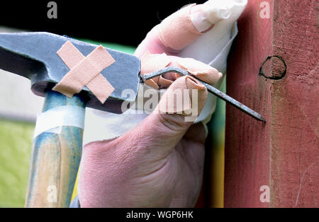 Close-up de la mano lesionada martillando clavos en madera