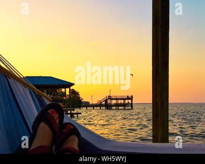 Bajo la sección de mujer relajándose en una hamaca en la playa contra el cielo durante la puesta de sol