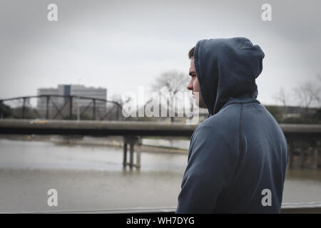 Joven llevaba chaqueta con capucha mientras está de pie por el Río Contra el cielo