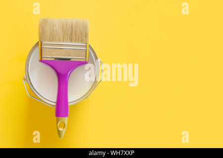 Pincel púrpura con abrir la lata de pintura blanca sobre fondo amarillo. Reparaciones de tendencia concepto. Vista desde arriba.