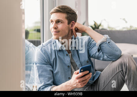 Mitad hombre adulto sentado por la ventana, utilizando el smartphone Foto de stock