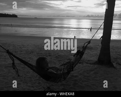 Silueta Joven relajándose en una hamaca en la playa durante el anochecer