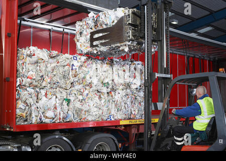 Trabajador en carretilla elevadora cargando las pilas de papeles reciclados en camión Foto de stock