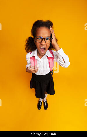 Pequeña niña de la escuela gritando tocando la cabeza sobre fondo amarillo
