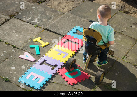Un alto ángulo de visualización de Boy montando triciclo por un texto sobre la acera