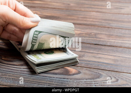 Vista en perspectiva de una empresaria de manos contando billetes de cien dólares sobre fondo de madera. Concepto de riqueza y éxito. Foto de stock