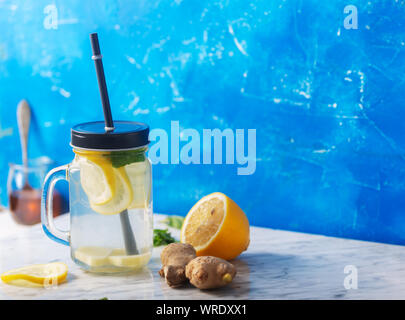 El agua en la jarra de cristal de jengibre con limón y miel sobre fondo azul con espacio de copia