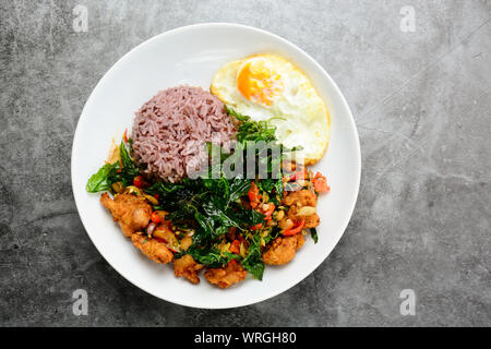 Pollo cocinado con el verde de la albahaca, servido con arroz cocido y huevo frito, caliente y picante del plato con hojas de albahaca. Foto de stock