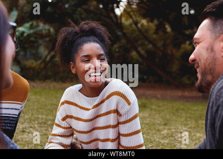 Retrato de una sonriente joven africana, sentarse y disfrutar con sus amigos en el parque