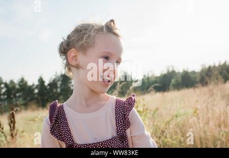 Retrato de una joven chica sonriente caminando a través de una pradera al atardecer
