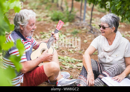 Par de caucásico adult senior permanecer juntos en las actividades de ocio al aire libre jugando un ukulele guitarra haciendo serenatas para la dama, el amor y el concepto eternamente junto con un par de gente guapa Foto de stock