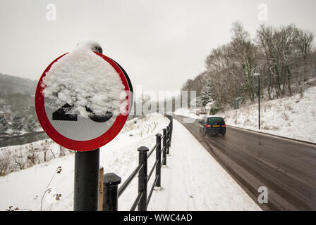 Señal de límite de velocidad oculta parcialmente por la nieve como coche velocidades pasado en condiciones resbaladizas.