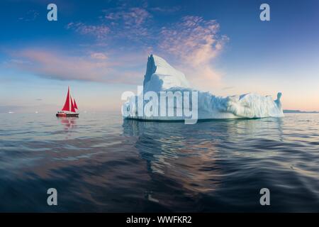 Rojo poco velero navegando entre témpanos flotantes en la bahía Disko glaciar sol de medianoche durante la temporada de verano polar. Ilulissat, Groenlandia. La Unesco Foto de stock