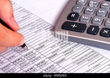 Empresario haciendo cuentas junto a una calculadora. Foto de stock
