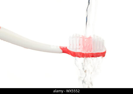 Agua cayendo sobre un cepillo de dientes rojo contra el fondo blanco. Foto de stock