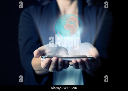 Detalle de las manos de una mujer sujetando un teléfono móvil desde el cual un holograma de un global está proyectado. Fotografía que muestra el concepto de la utilización de tecnologías Foto de stock