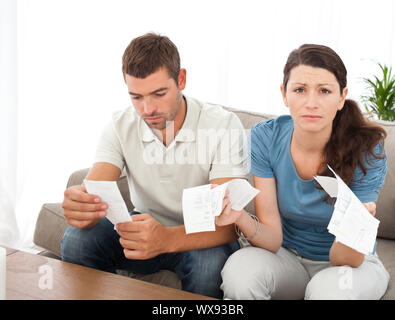 Mujer desesperada haciendo sus cuentas con su novio sentado en el sofá en casa Foto de stock