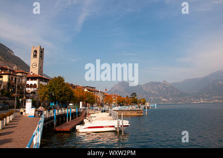 Paseo Costanera a Tavernola bergamasca, en el lago de Iseo, Lombardía, Italia con barcos amarrados y la histórica torre del reloj en una ciudad en la costa lo Foto de stock