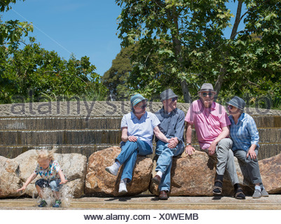 Los abuelos sentados en el parque y nieto chapoteando en el agua