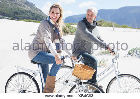 Despreocupada par ir en un paseo en bicicleta en la playa, sonriendo a la cámara