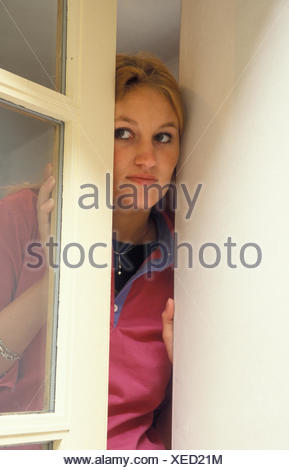 Mujer joven mirando sospechosamente fuera de la ventana