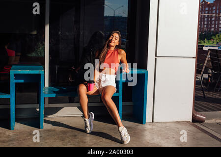 Heureux élégant jeune brunette woman wearing white shorts et baskets rose holding tasse de café d'aller. Banque D'Images