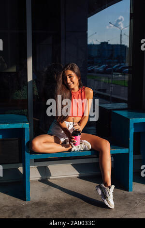 Heureux élégant jeune brunette woman wearing white shorts et baskets rose holding tasse de café d'aller. Banque D'Images